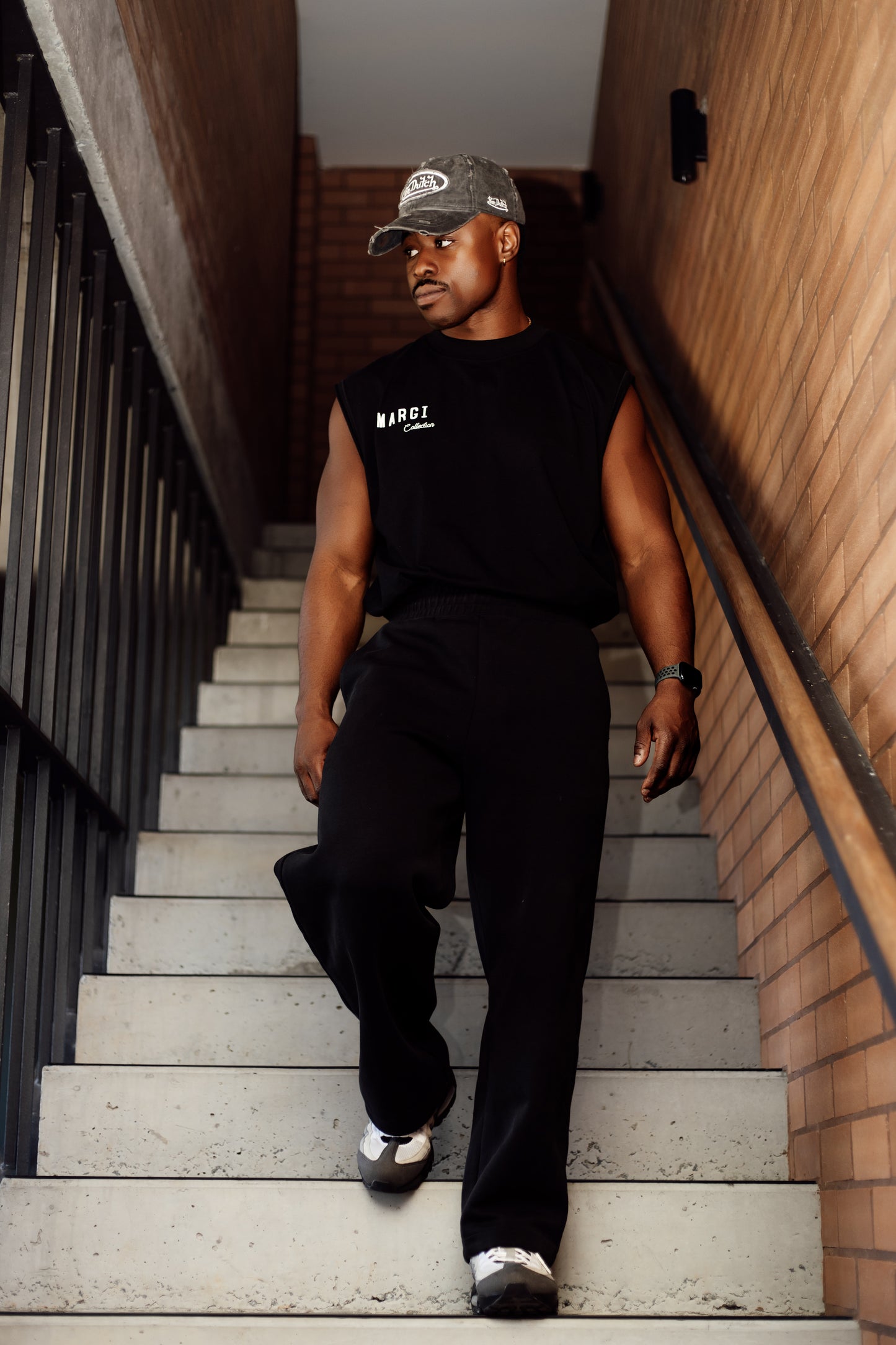 Man in black sleeveless shirt and pants walking up a set of stairs.