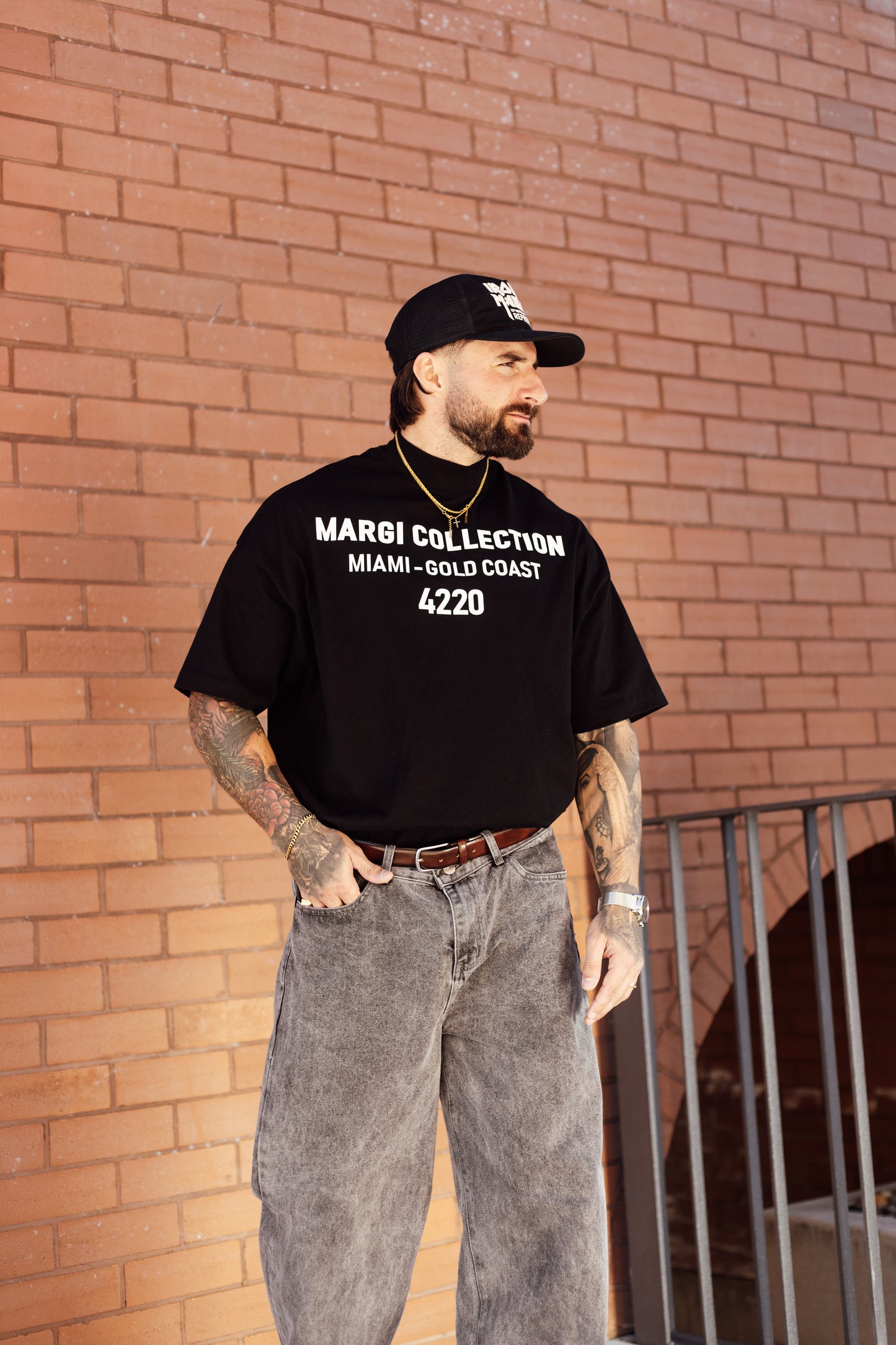 Man wearing a black t-shirt with text, standing against a brick wall.