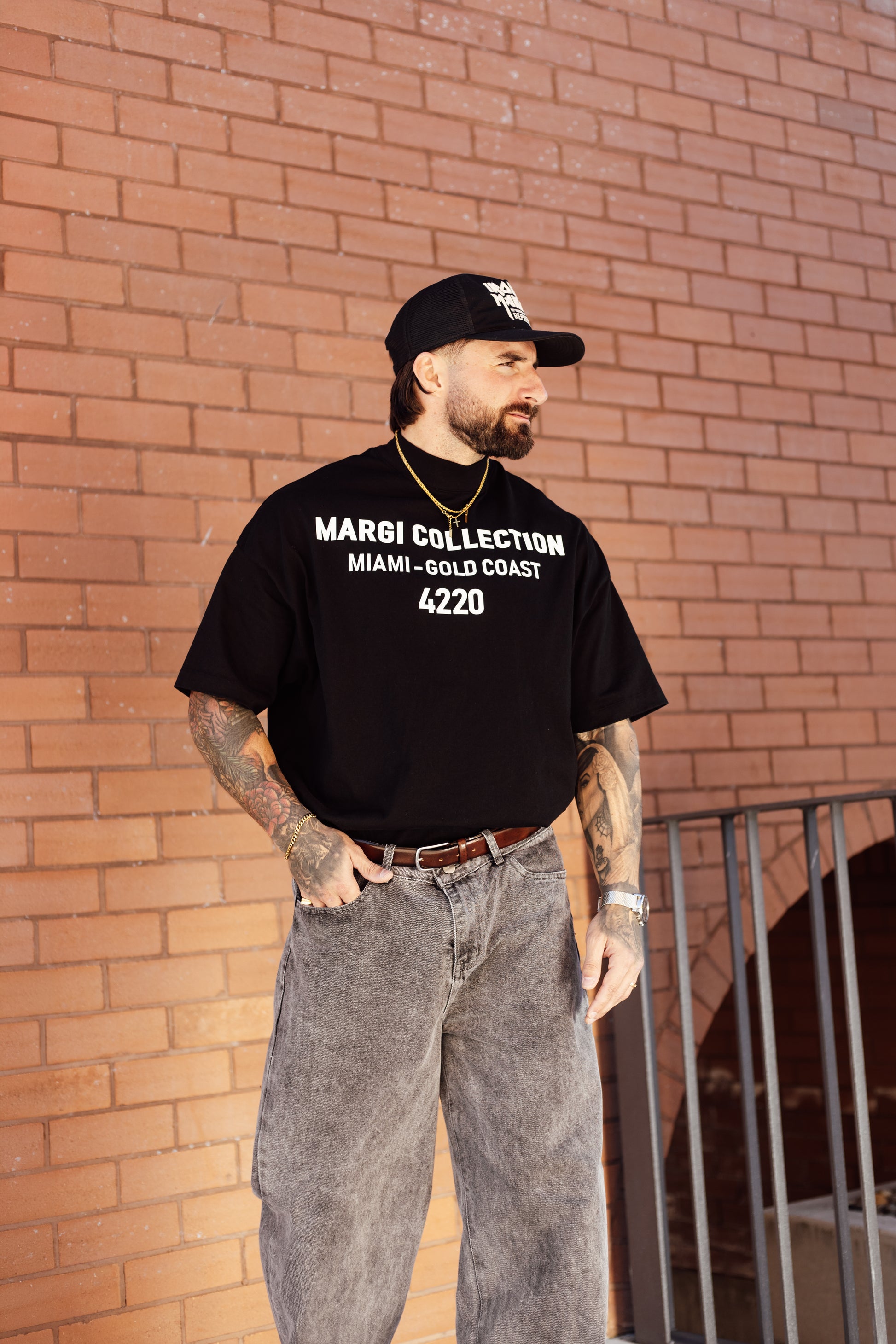 Man wearing a black t-shirt with text, standing against a brick wall.