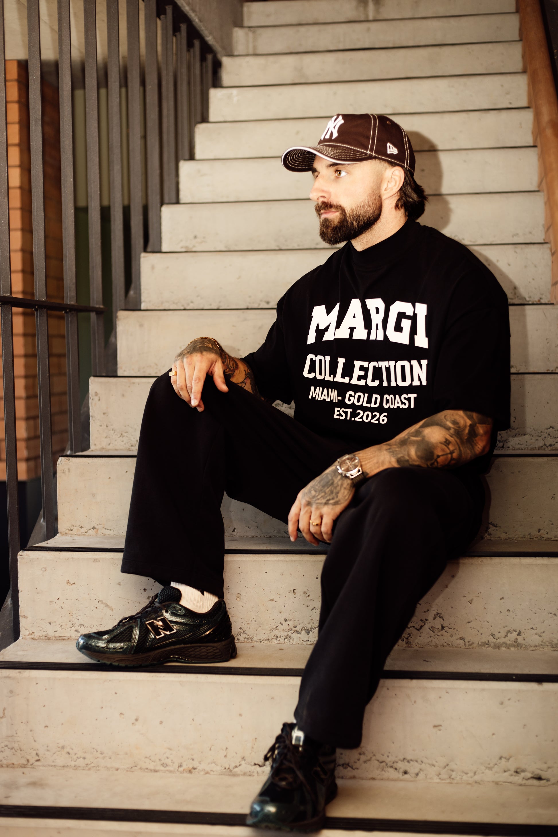 Man sitting on stairs wearing a black 'MARGI COLLECTION' tshirt