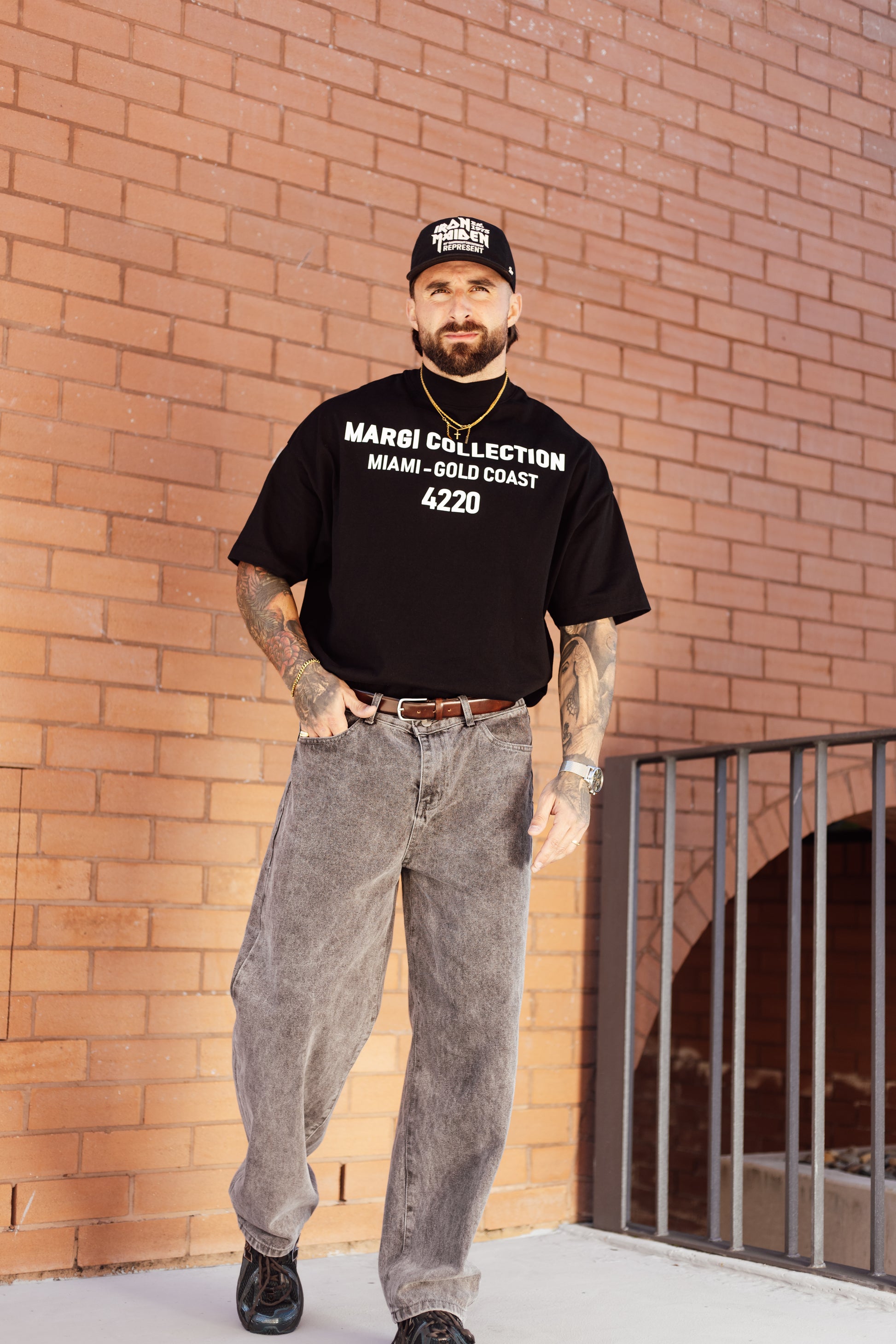 Man wearing a black t-shirt with text, standing against a brick wall.